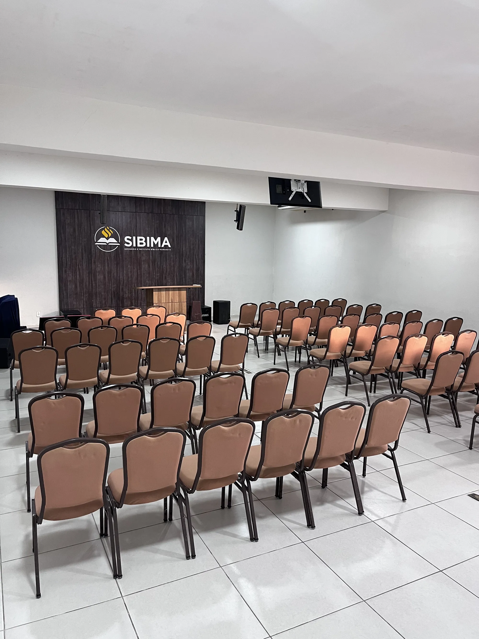 Auditório do SIBIMA com cadeiras dispostas para o culto e o logotipo do seminário ao fundo